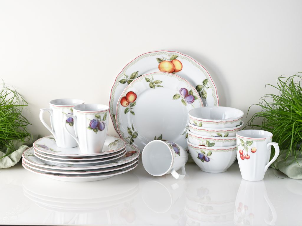A collection of porcelain dinnerware with fruit motifs, including plates, bowls, and mugs, arranged on a white surface.
