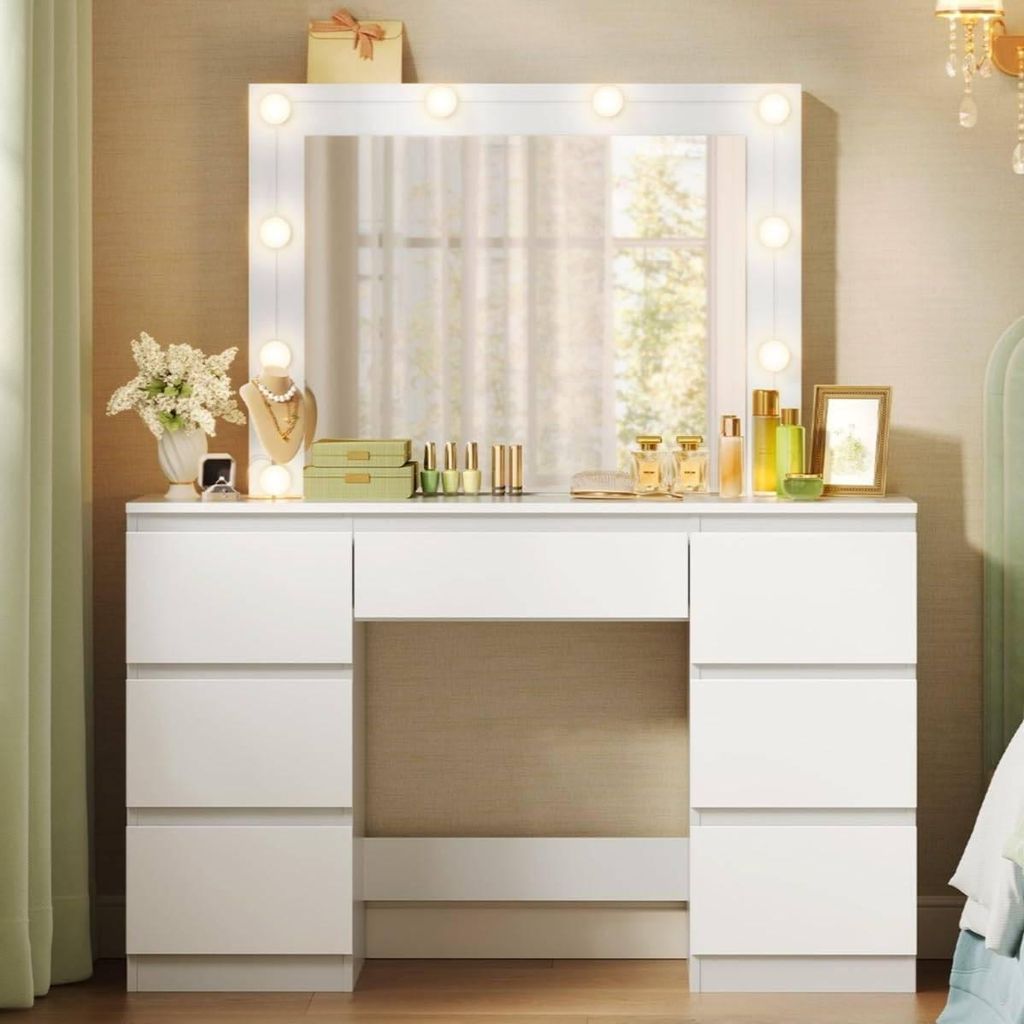 A white vanity table with a lighted mirror and various makeup items on top, set in a bedroom.