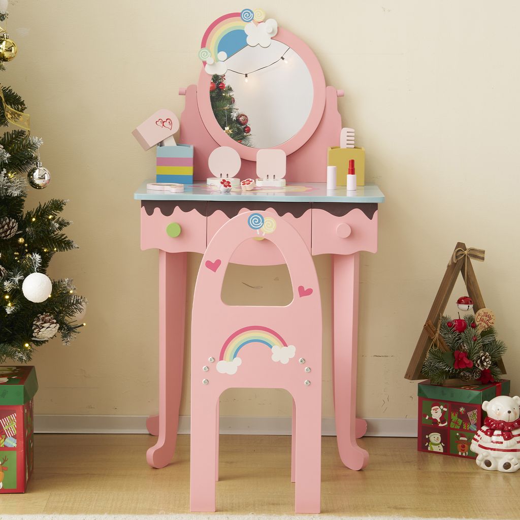 A pink children's vanity table and stool set decorated with rainbows and clouds, placed next to a decorated Christmas tree.