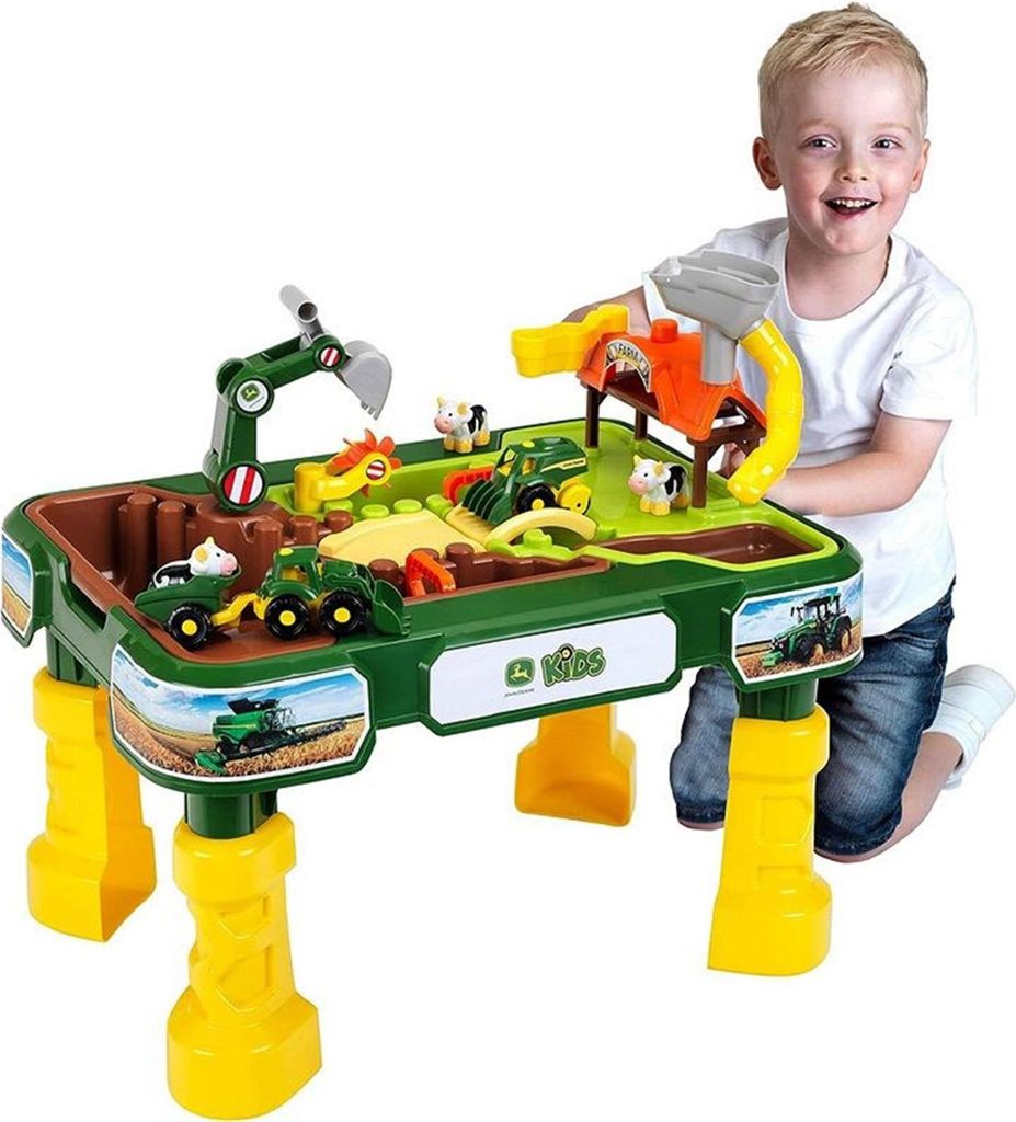 A young boy is playing with a John Deere farm-themed sand and water play table.