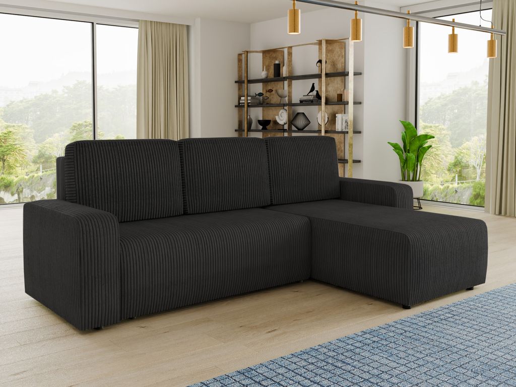 A dark grey sectional sofa is shown in a well-lit living room with large windows and a bookshelf in the background.