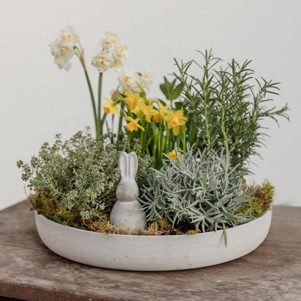 A decorative bowl filled with plants and a small bunny figurine.