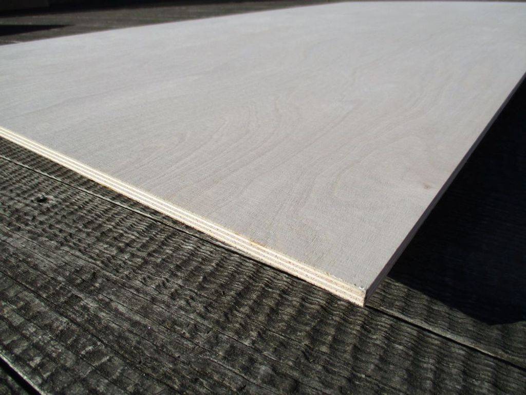 A close-up, angled view of a light-colored plywood sheet resting on a dark, textured surface.