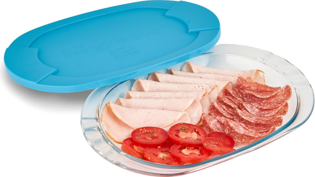 A glass serving dish filled with sliced meats and tomatoes, with a blue lid placed next to it.