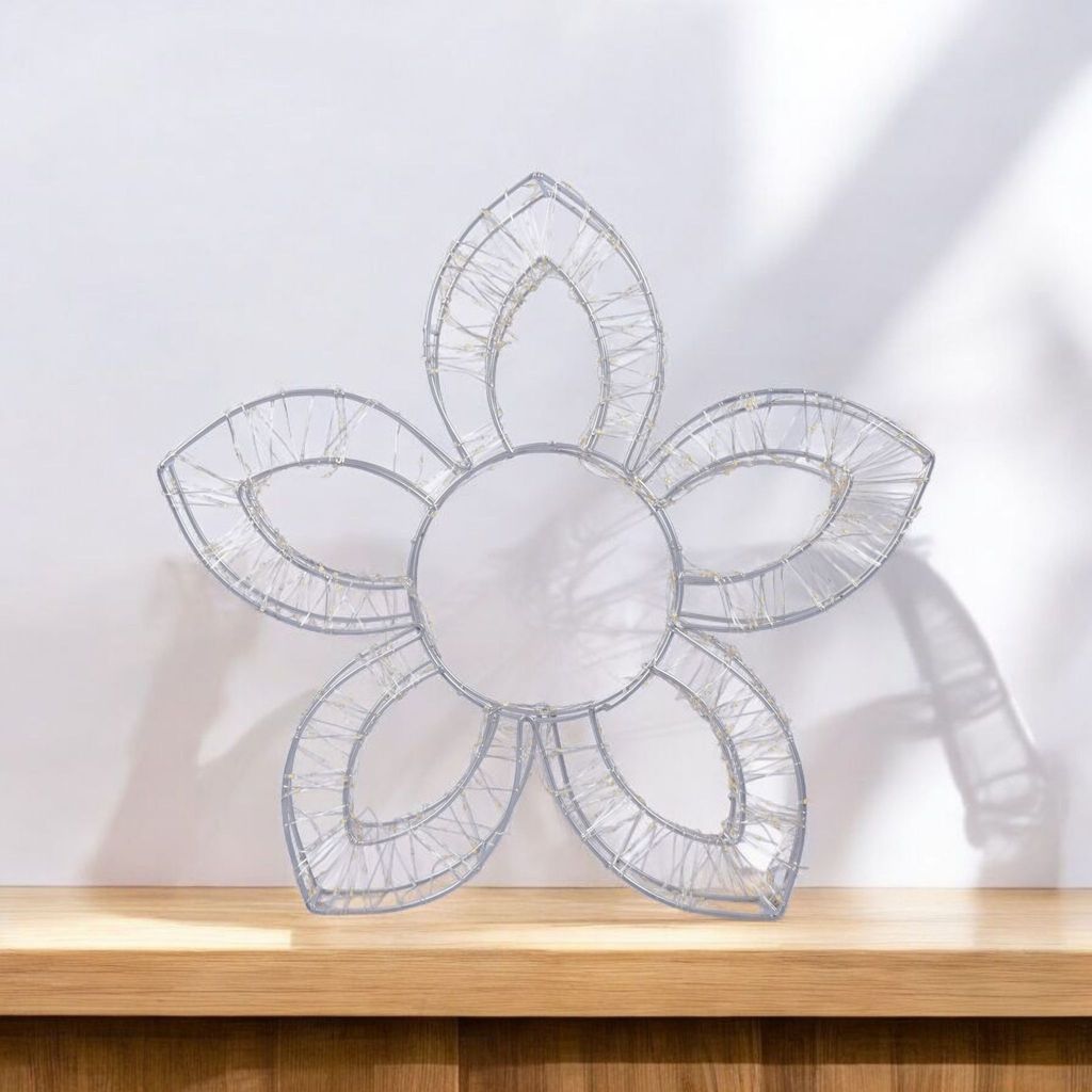 A decorative flower lamp is placed on a wooden shelf against a white wall.