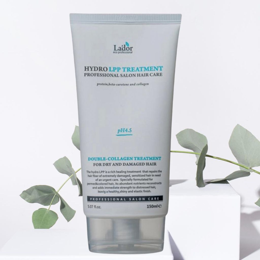 A tube of Lador Hydro LPP Treatment hair care product is displayed on a white pedestal, with green eucalyptus leaves in the foreground and background.