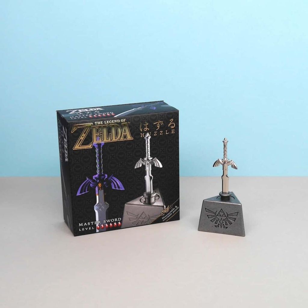 Master Sword Metallpuzzle aus The Legend of Zelda mit Verpackung; Miniatur-Schwert im Sockel vor hellblauem Hintergrund