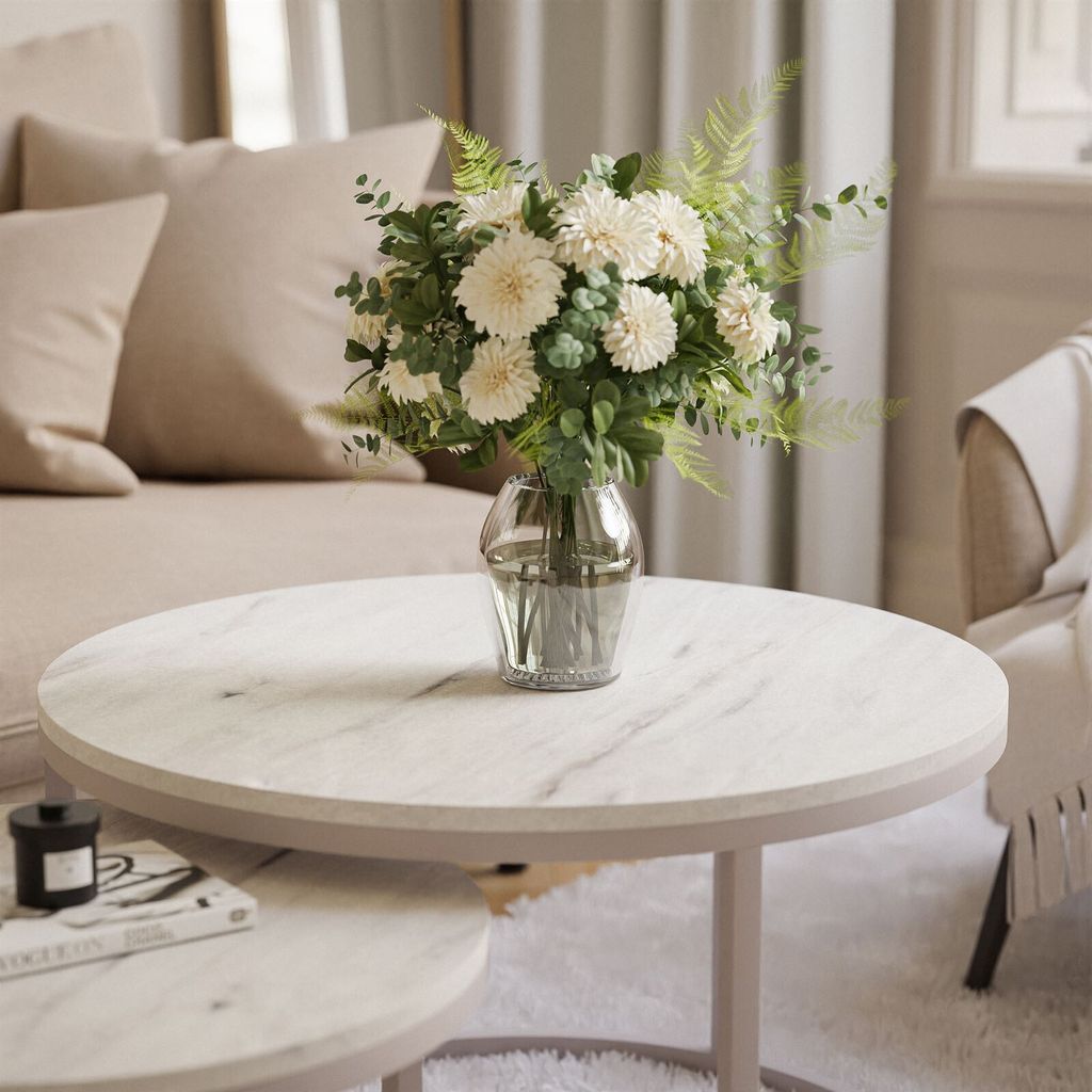 A floral arrangement in a glass vase sits on a marble coffee table in a living room.