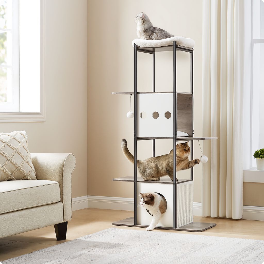 Three cats are playing on a multi-level cat tree in a living room setting.