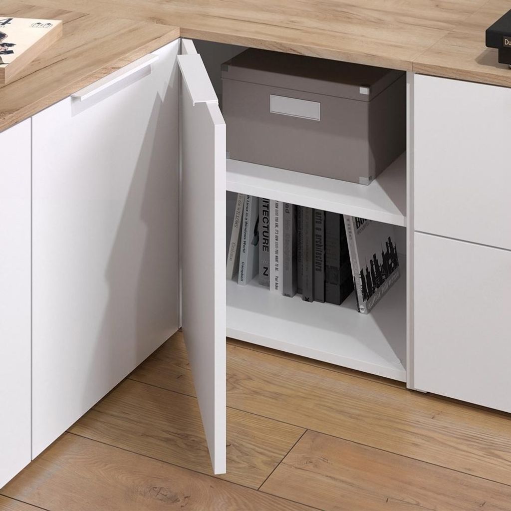 A close-up view of a white corner cabinet with a wood-tone countertop, showing an open door revealing shelves with books and a storage box.