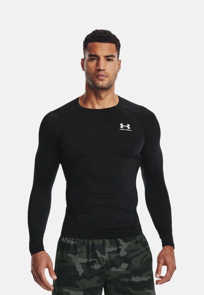 A man wearing a black long-sleeved shirt and camouflage shorts against a white background.