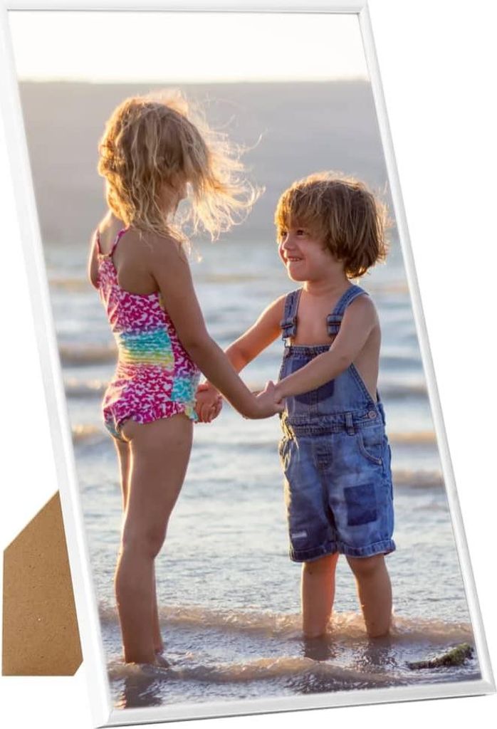 Two children standing in shallow water at the beach, holding hands.