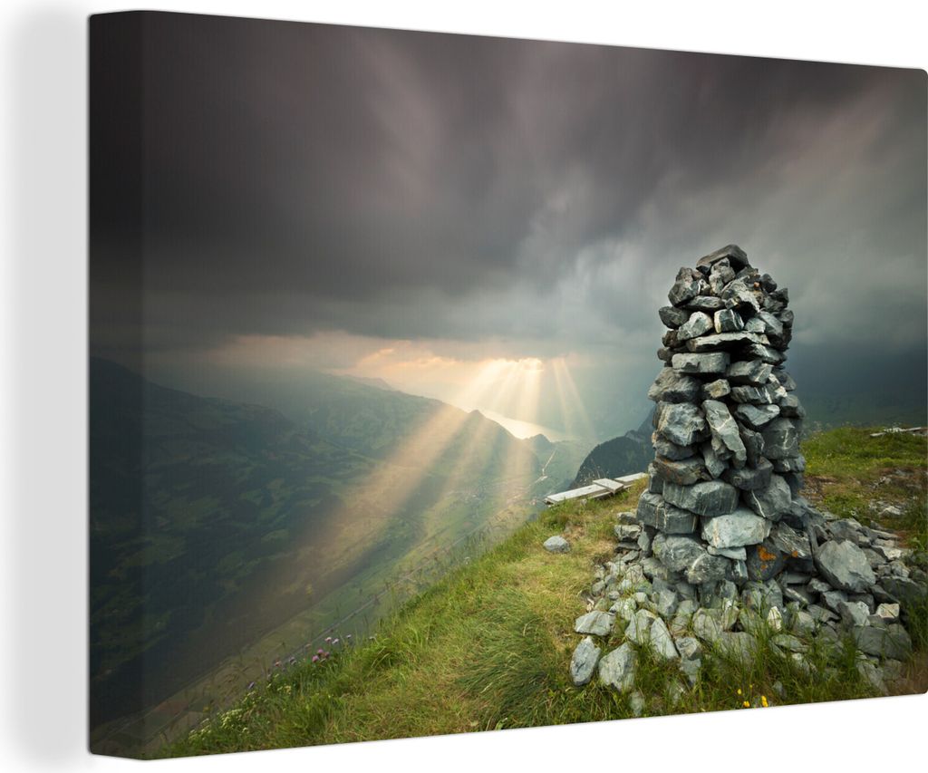 OneMillionCanvasses - Leinwandbilder - 140x90 cm, Ein Steinhaufen auf einem Berggipfel mit dunklen Wolken und Sonnenstrahlen, Wandbilder Kunstdru...