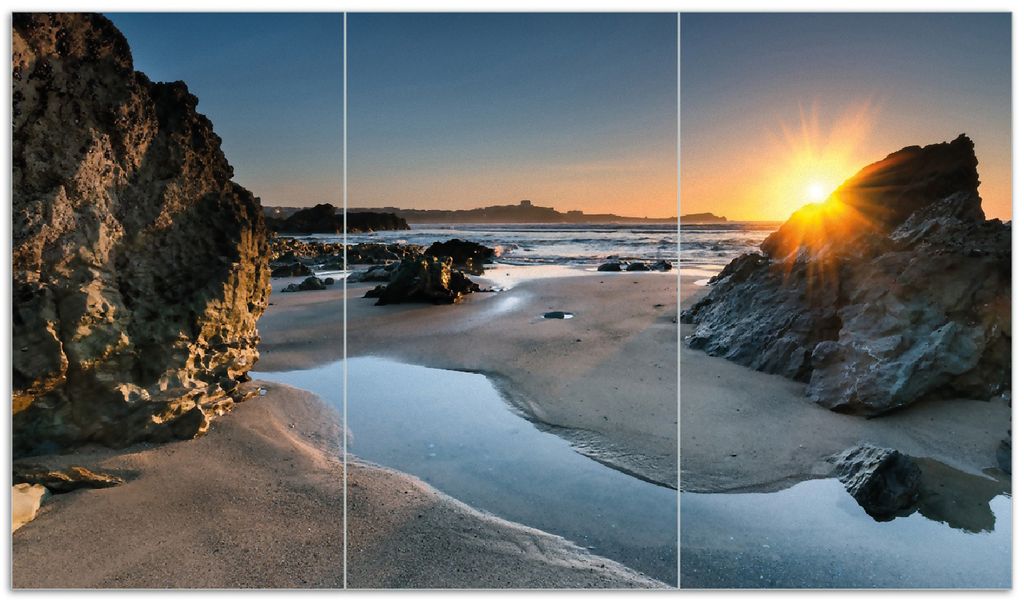 Wallario Herdabdeckplatte aus Glas, Größe 90 x 52 cm 3-teilig, Motiv Sonnenuntergang hinter einem Felsen am Strand
