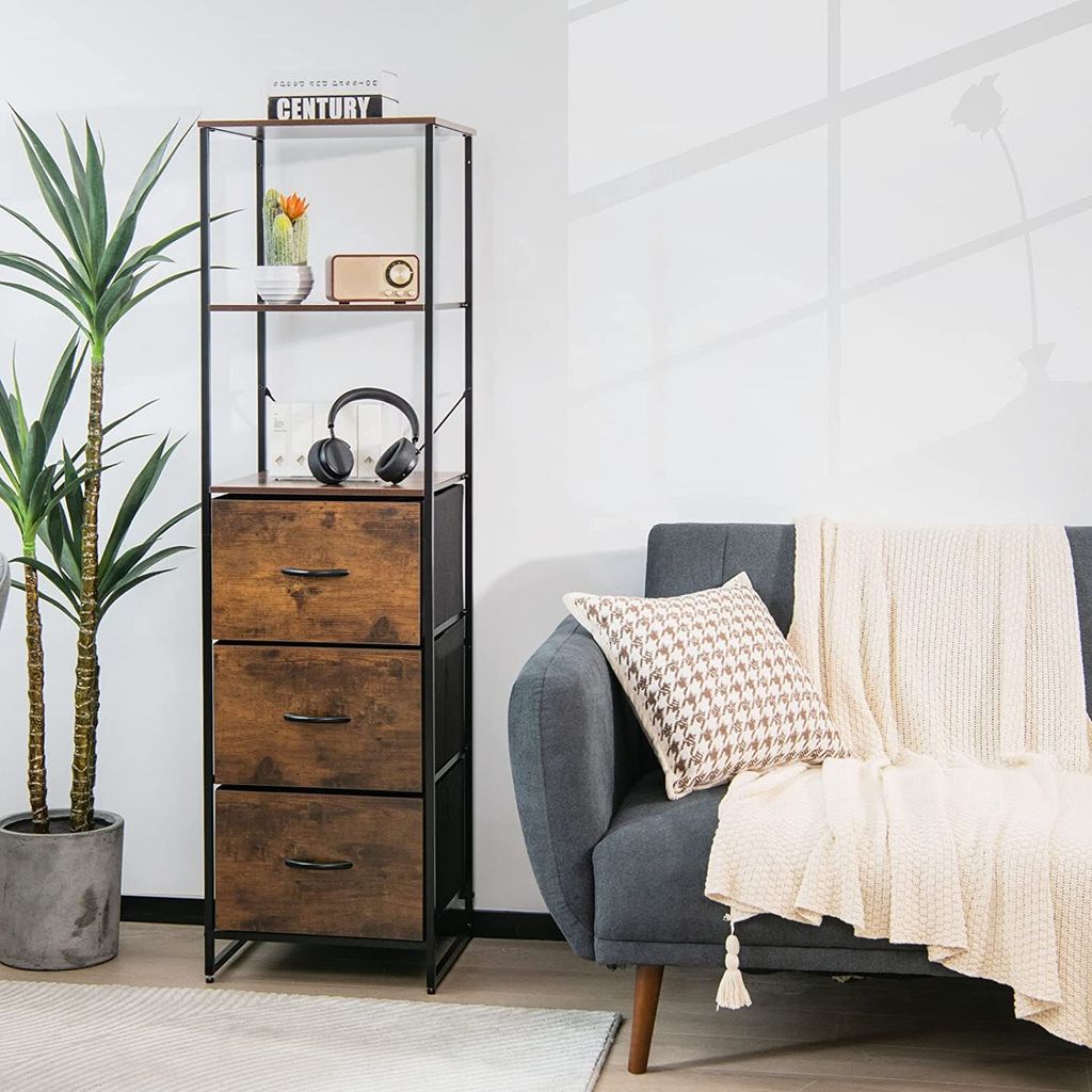 A tall storage cabinet with three drawers and three shelves is placed next to a sofa with a throw blanket and a pillow.