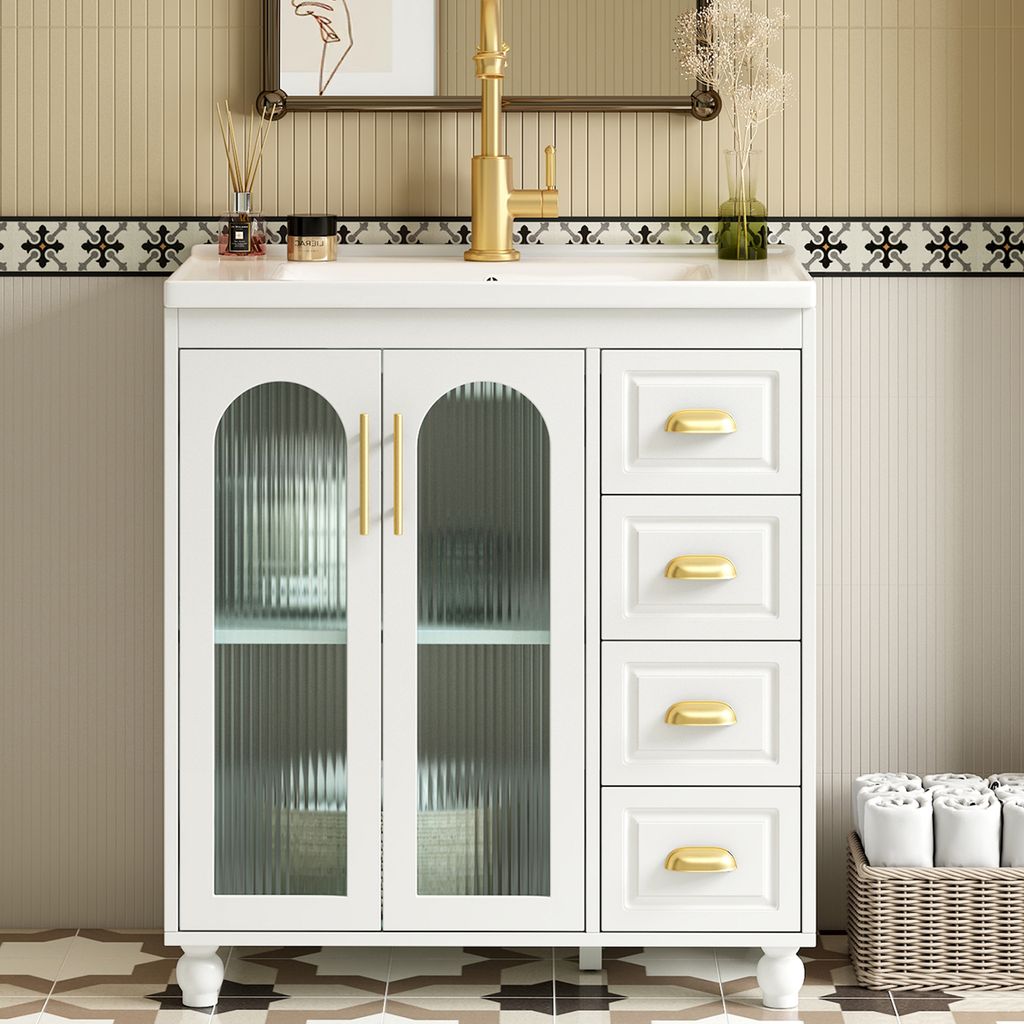 A white bathroom vanity with glass doors and gold hardware, set against a tiled wall.