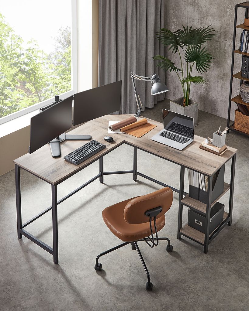 An L-shaped desk with two monitors, a laptop, keyboard, and an office chair in a home office setting.