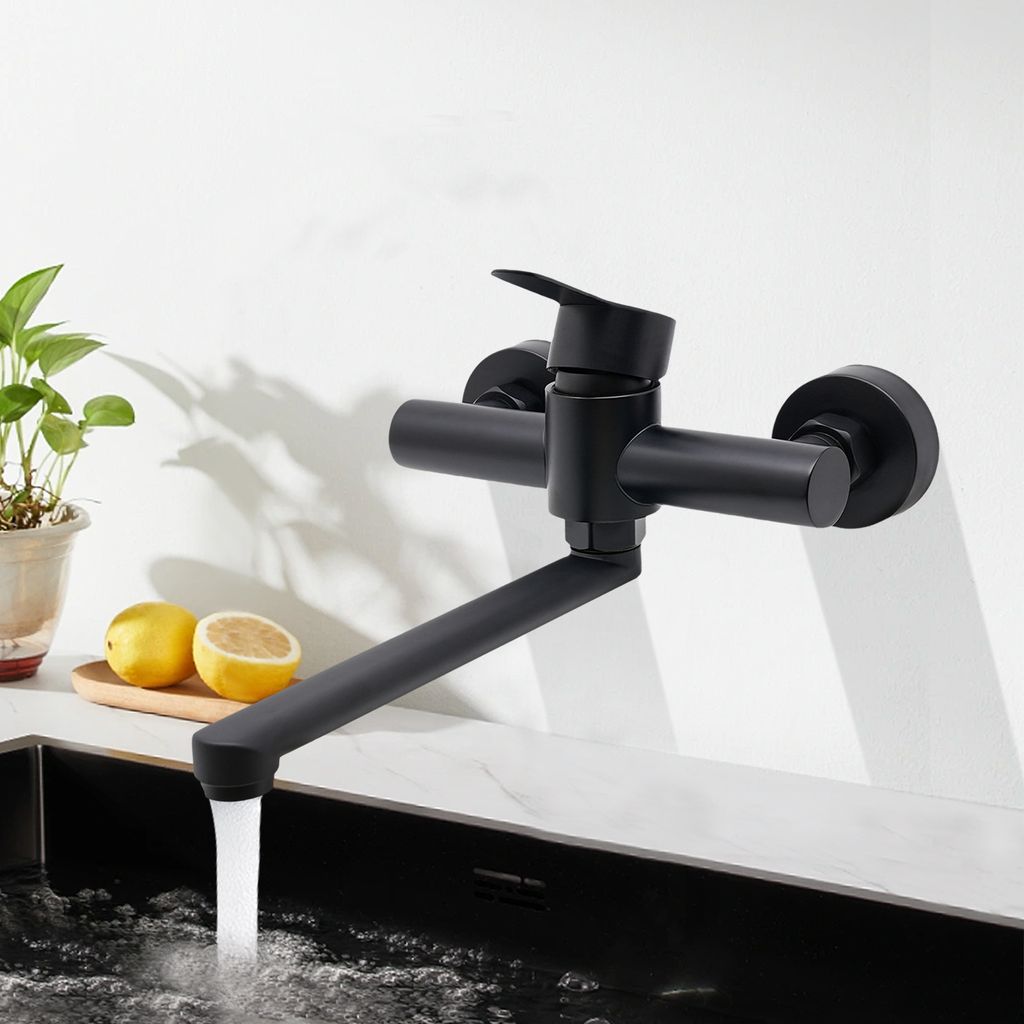 A black kitchen faucet mounted on a white wall above a sink, with water running.