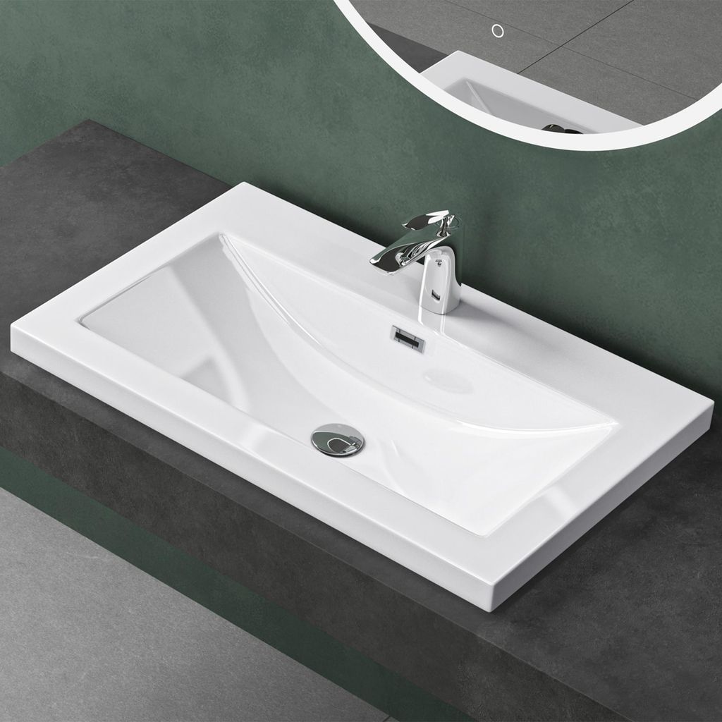 A white rectangular sink with a chrome faucet is installed on a dark gray countertop against a dark green wall.
