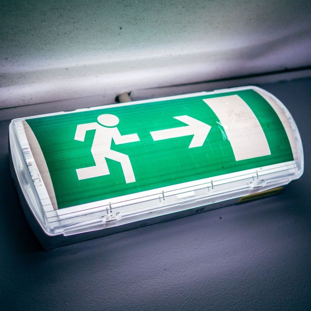 A close-up shot of a green LED emergency exit sign with a white running man pictogram and arrow.