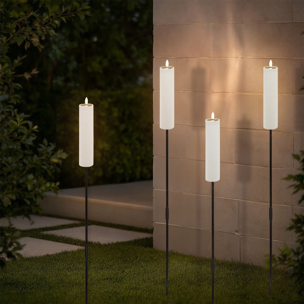 Four solar-powered candle-shaped lights are placed in a garden at dusk, illuminating a stone wall and surrounding greenery.