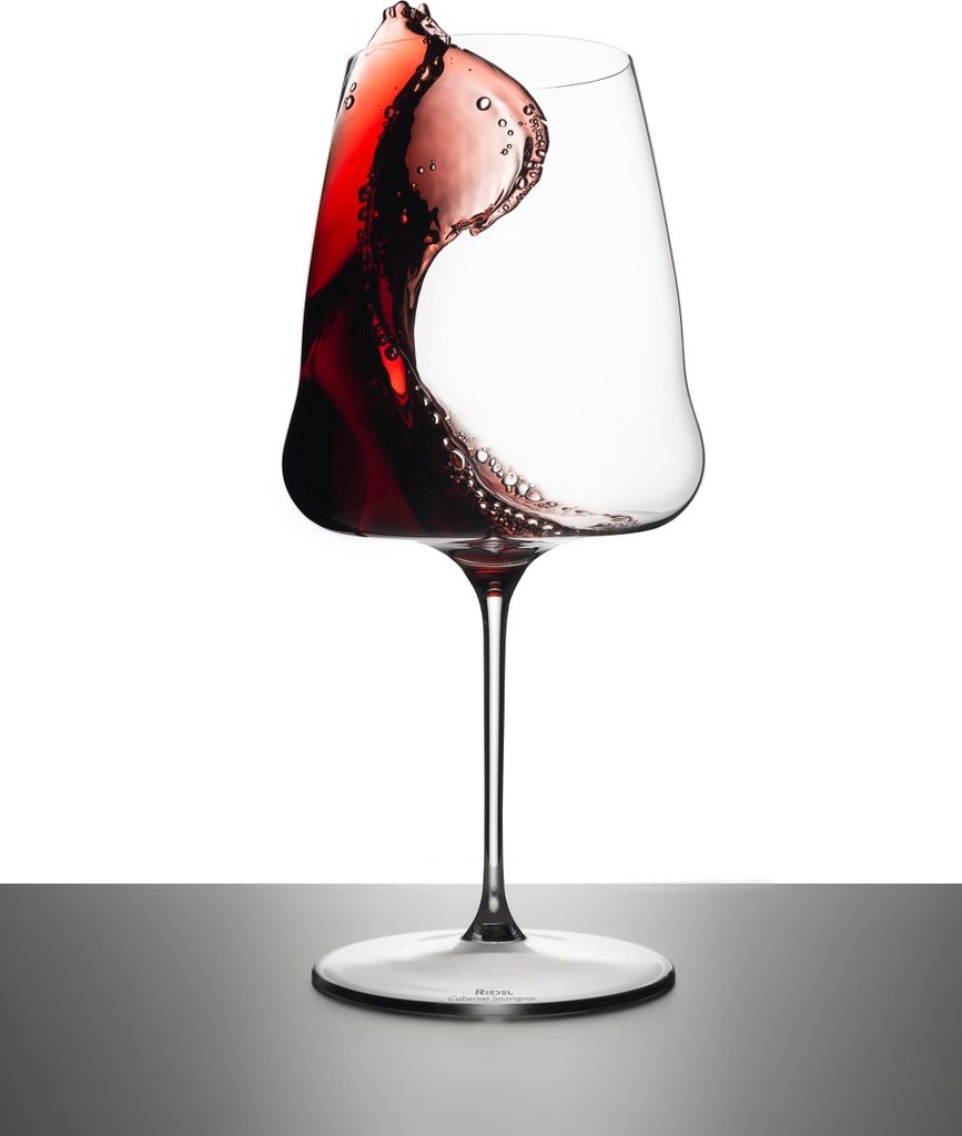 A wine glass with red wine splashing inside, set against a white background and on a dark surface.