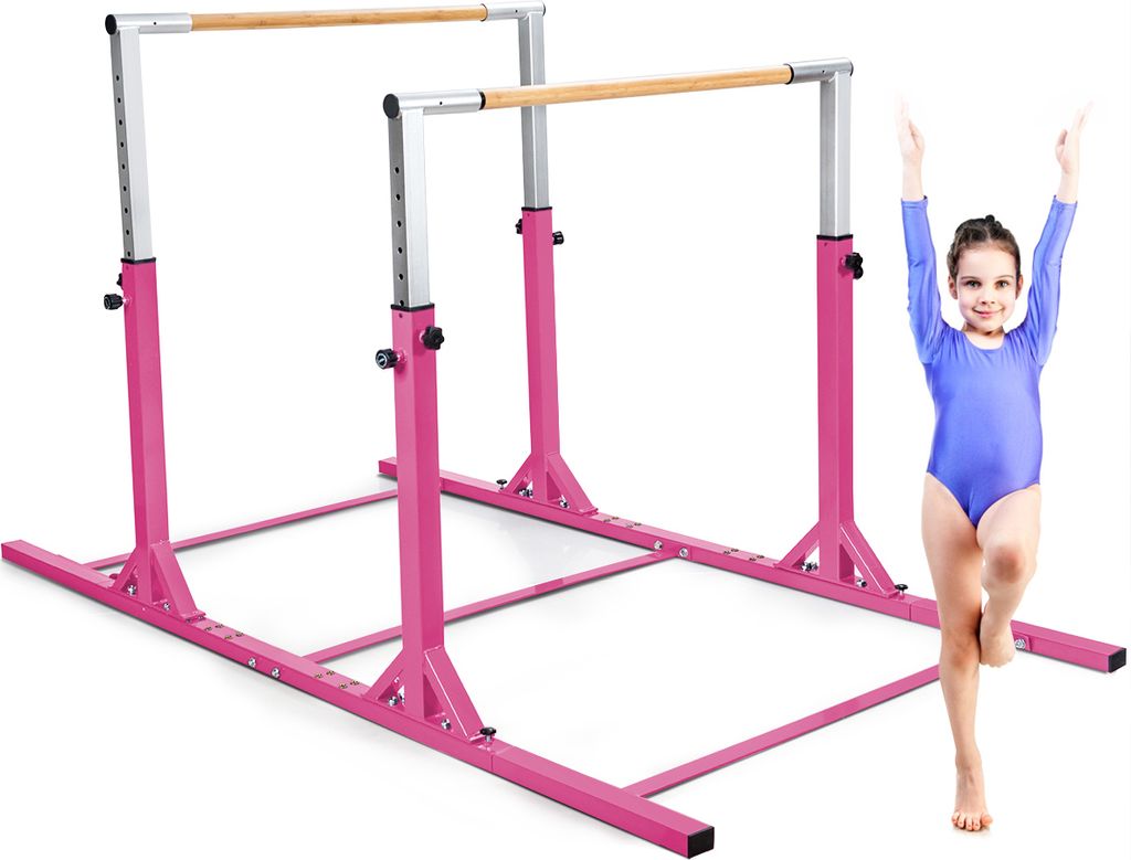A young girl in a blue leotard stands on one leg next to a pink gymnastics bar set.