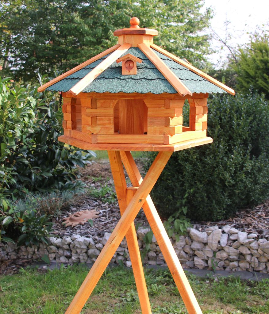 A wooden birdhouse on a stand in a garden setting.