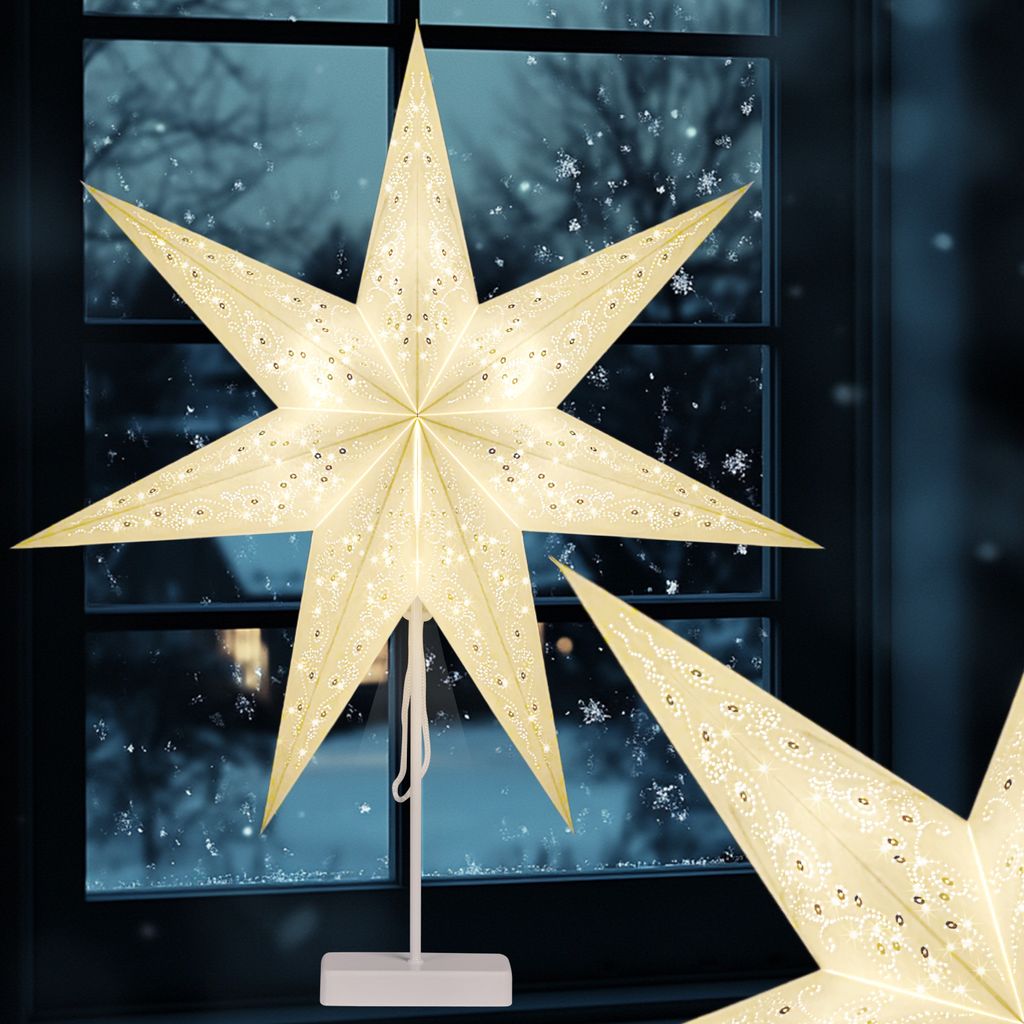 A lit-up star decoration is placed on a window sill with a snowy scene visible through the window.