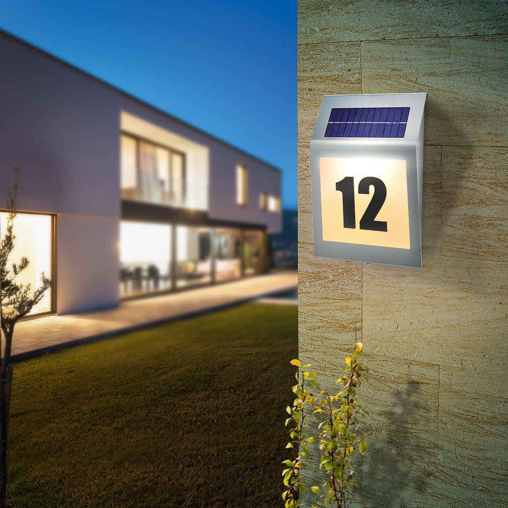 A modern house at dusk with a solar-powered house number light illuminated on the wall.