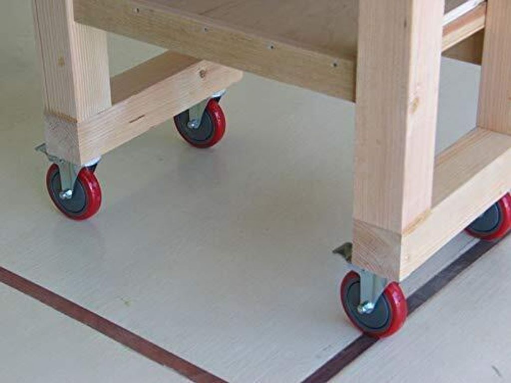 Close-up of the base of a wooden utility cart with casters on a light-colored floor.