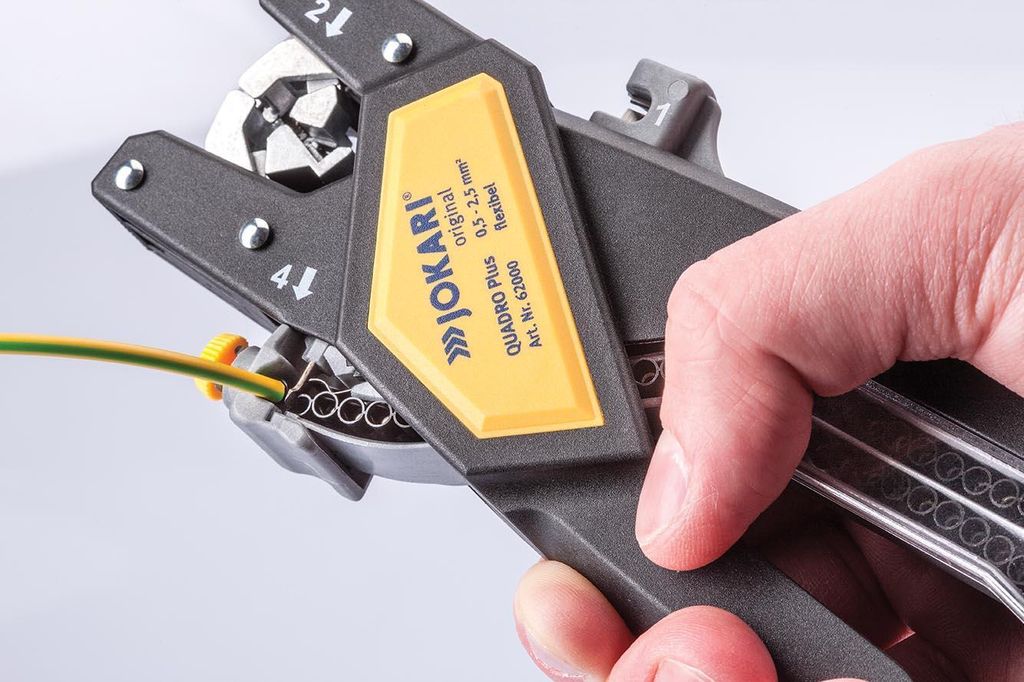 A hand is holding a wire stripping tool, with a wire being fed into it.