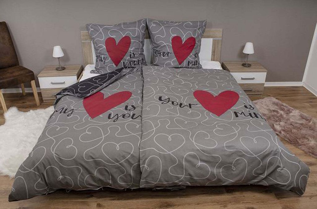 A bed with a duvet cover and pillows featuring a heart pattern and text.