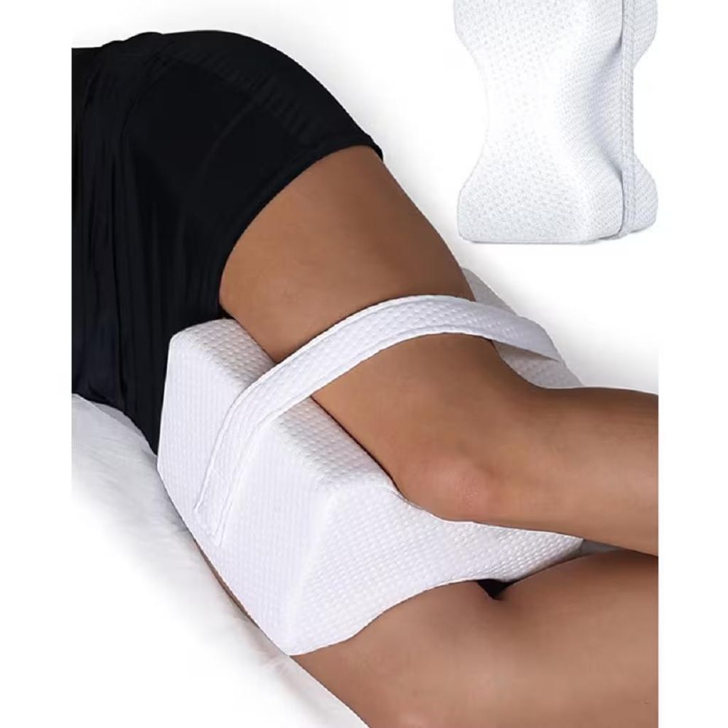 A person's leg is shown with a white knee pillow placed between the knees while lying down.
