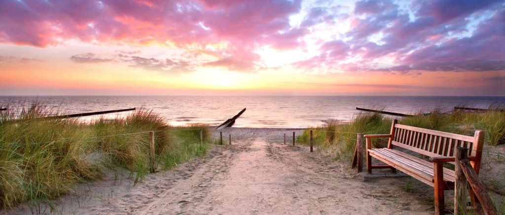 A tranquil beach scene at sunset with a wooden bench overlooking the ocean.