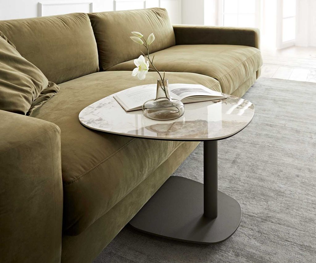 A modern living room scene featuring a green sectional sofa and a small, uniquely shaped side table with a marble-like top.