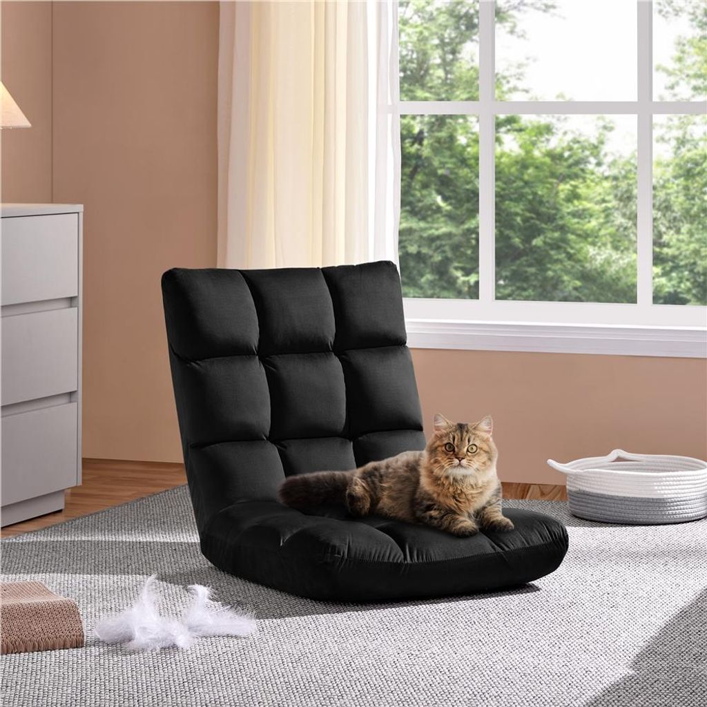 A black floor chair with a cat on it, placed in a room with a dresser and a window.