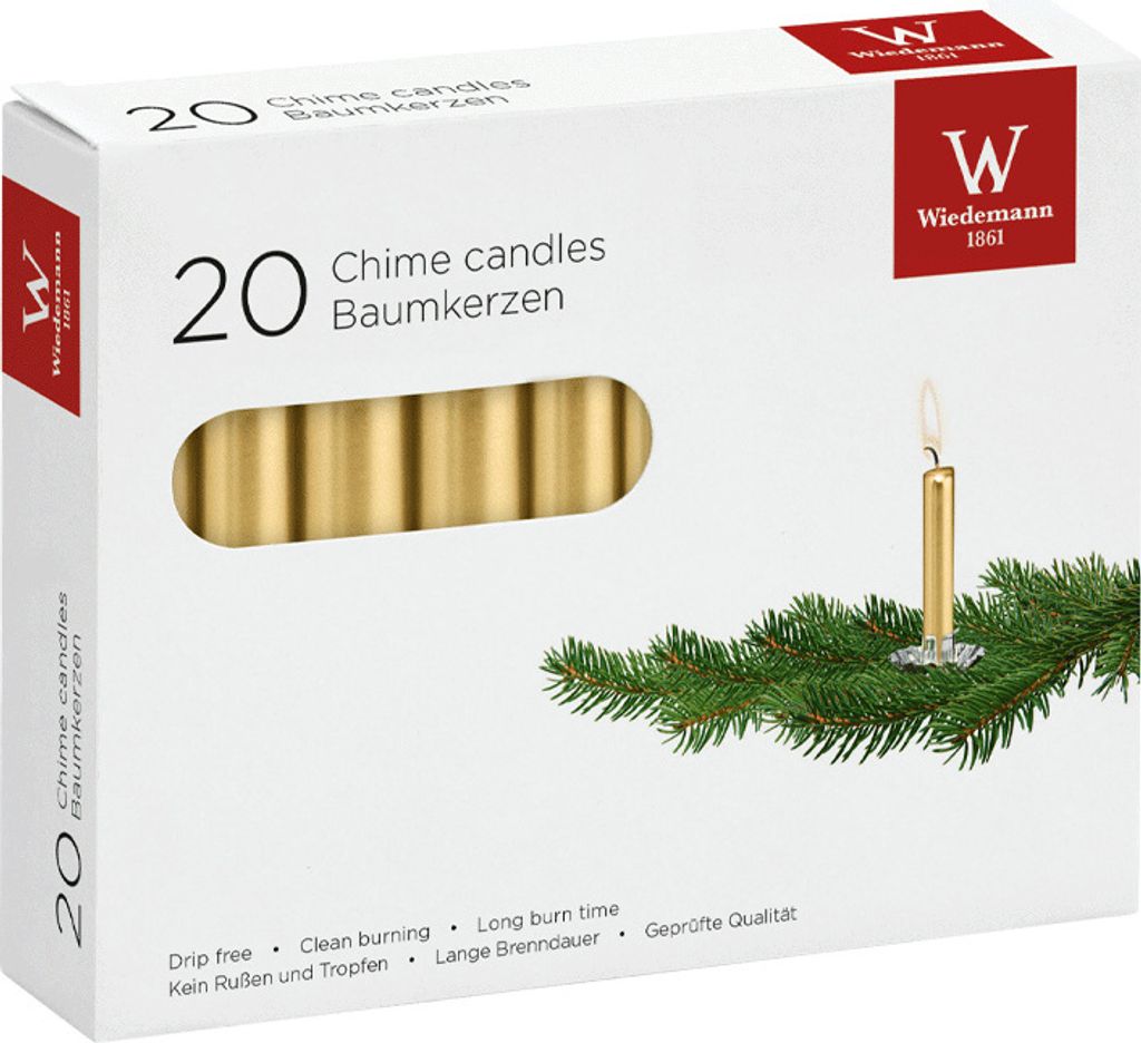 A box of gold chime candles with a sprig of evergreen branches and a single lit candle.