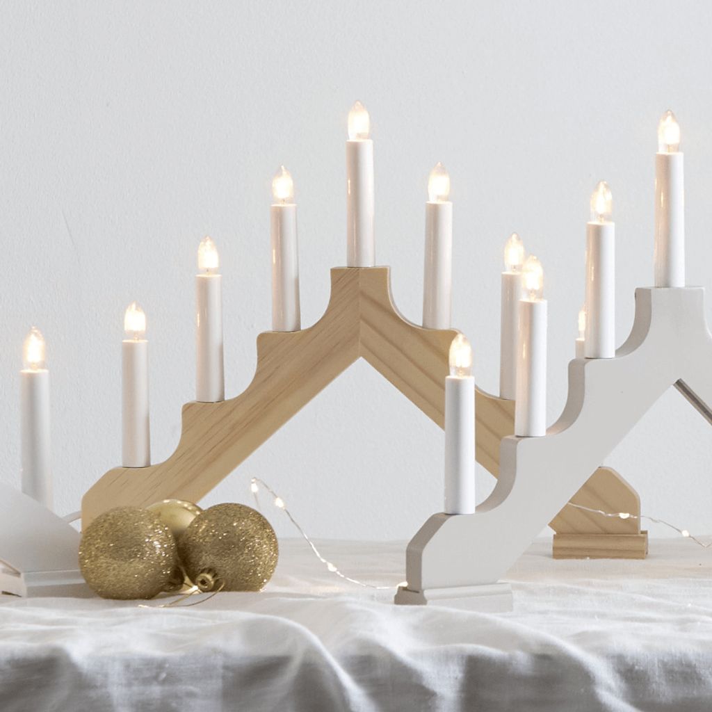 A close-up shot of two candle holders with lights on, placed on a white tablecloth with gold ornaments.