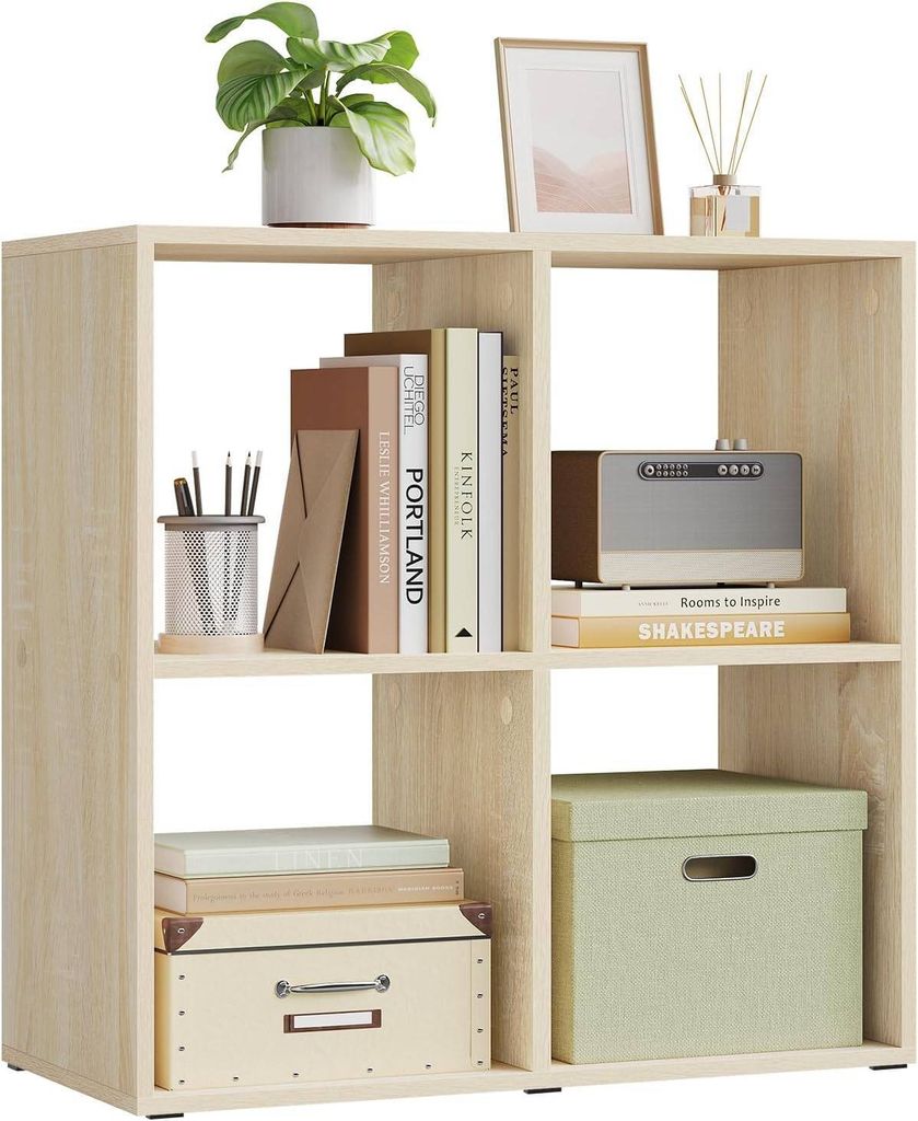 A light oak colored cube shelf unit with books, a plant, a picture frame, and storage boxes.