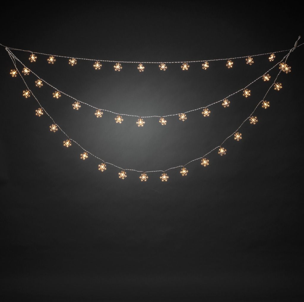 Three strings of snowflake-shaped LED lights are hung in a curved arrangement against a black background.