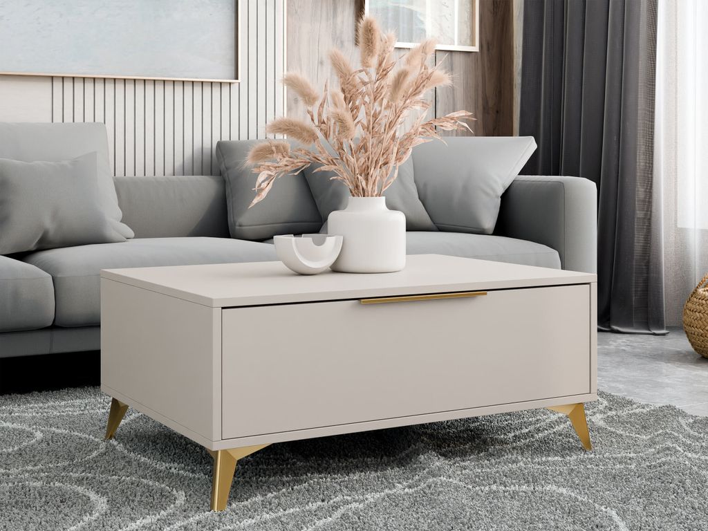 A modern living room scene featuring a coffee table with a drawer and gold metal legs, placed in front of a gray sofa. A vase with dried flowers sits on top of the table.