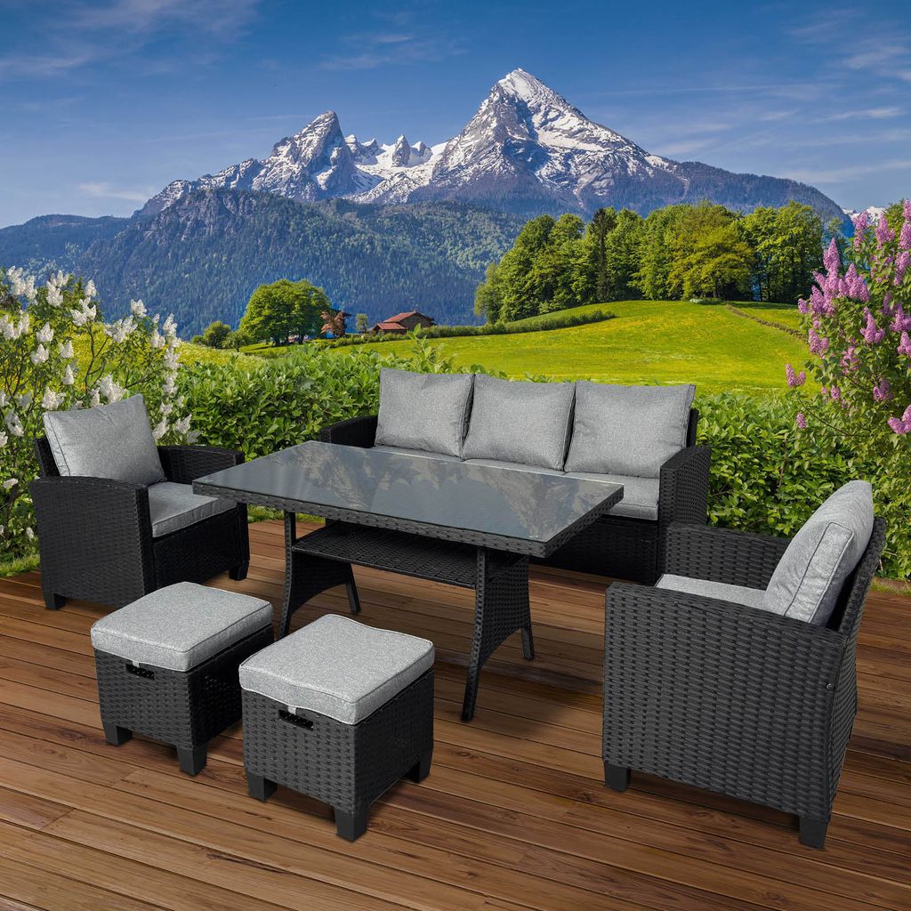 A polyrattan garden seating set is arranged on a wooden deck with a scenic mountain landscape in the background.