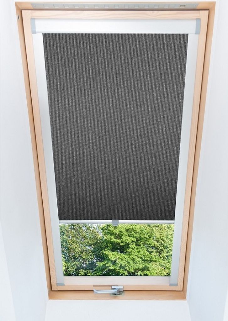 A dark gray roller blind is partially lowered over a skylight, revealing green trees and foliage outside.