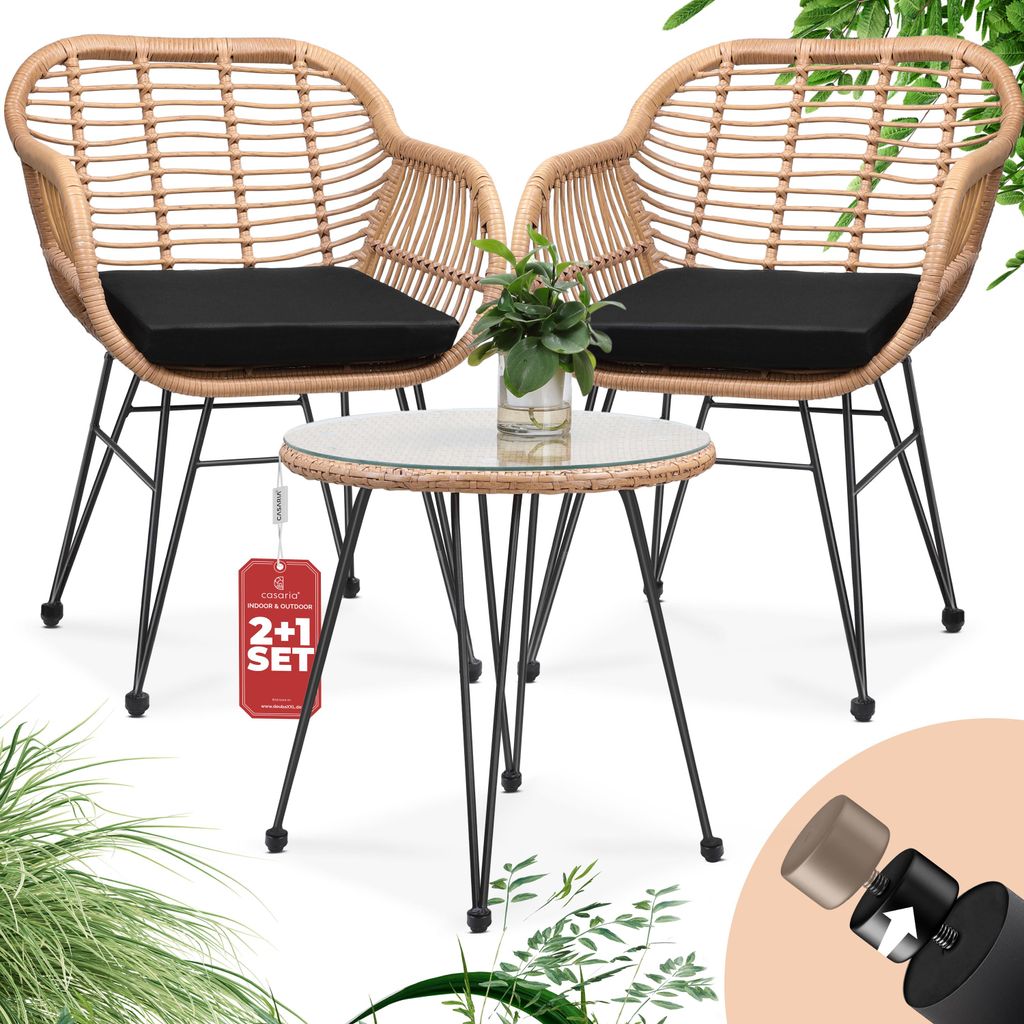 A rattan-look balcony set with two chairs and a small table, featuring black cushions and a glass tabletop. A small potted plant sits on the table. A red tag with "2+1 SET" is attached to the table.