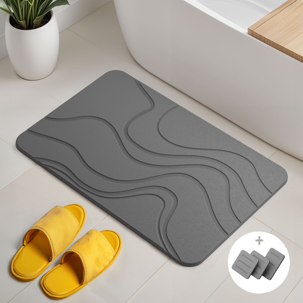A dark gray bath mat with a wavy pattern is placed on a tiled floor next to a bathtub. Two yellow slippers are in the foreground.