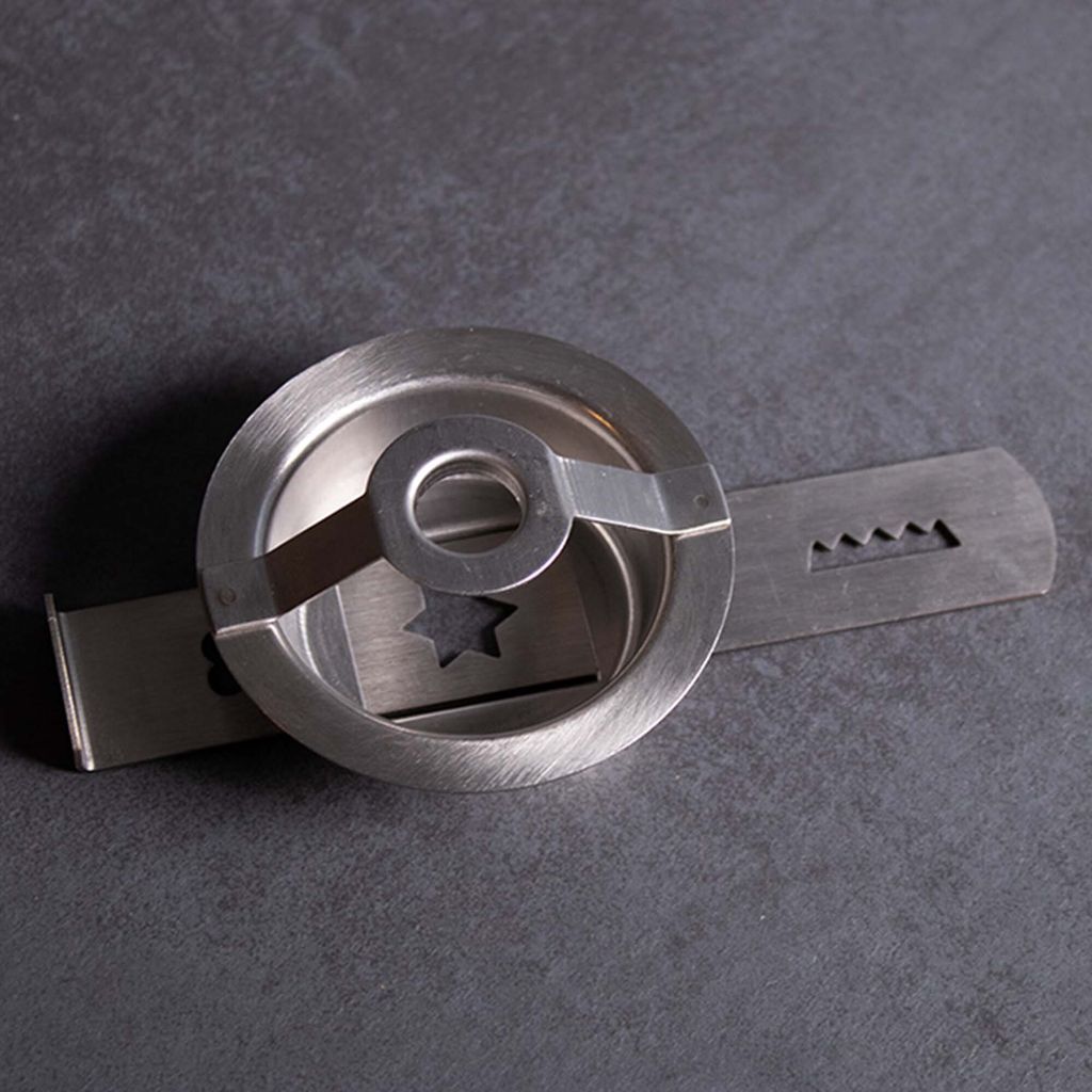 A close-up, angled view of a metal cookie press attachment on a dark gray surface.