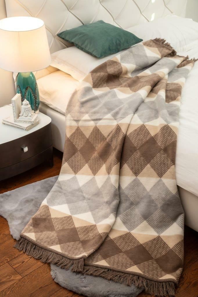 A blanket is draped over a bed next to a nightstand with a lamp.