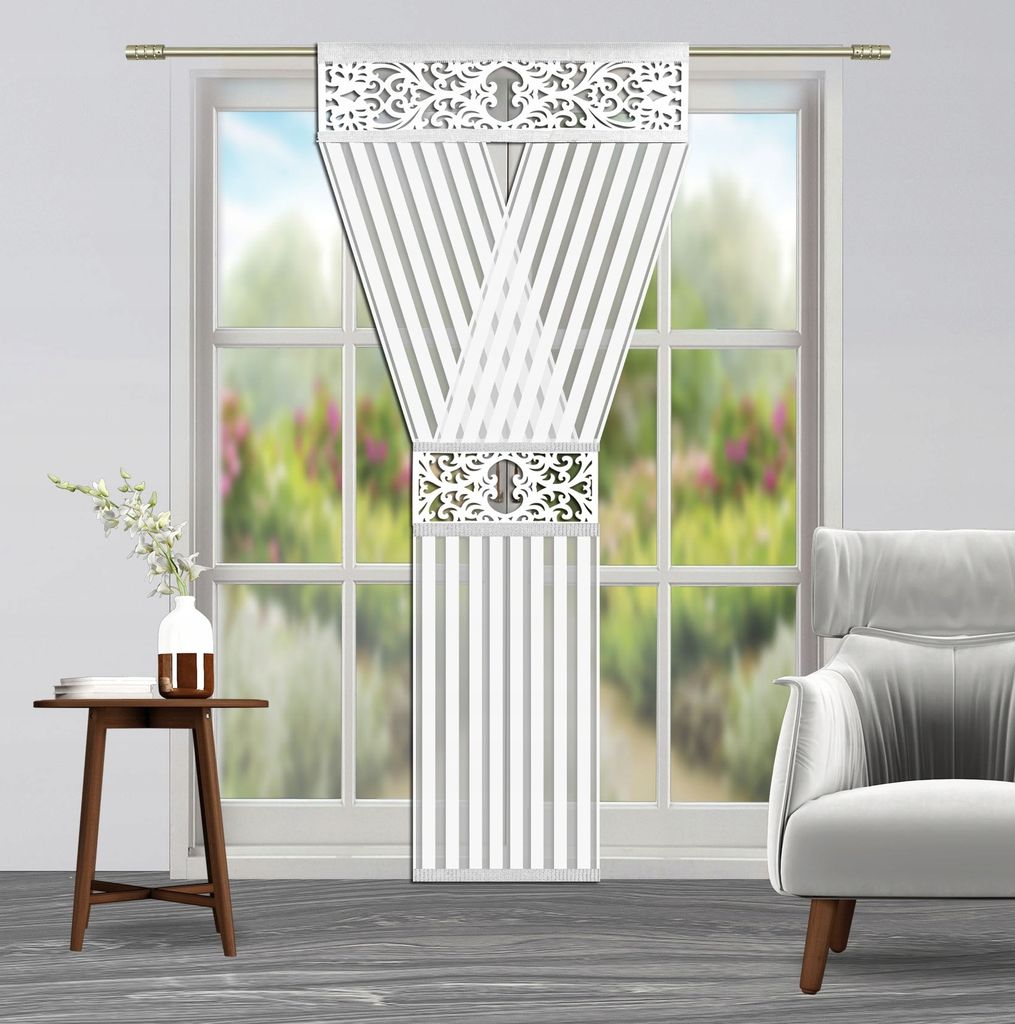 A decorative curtain panel hanging in a window with a small table and vase to the left and an armchair to the right.