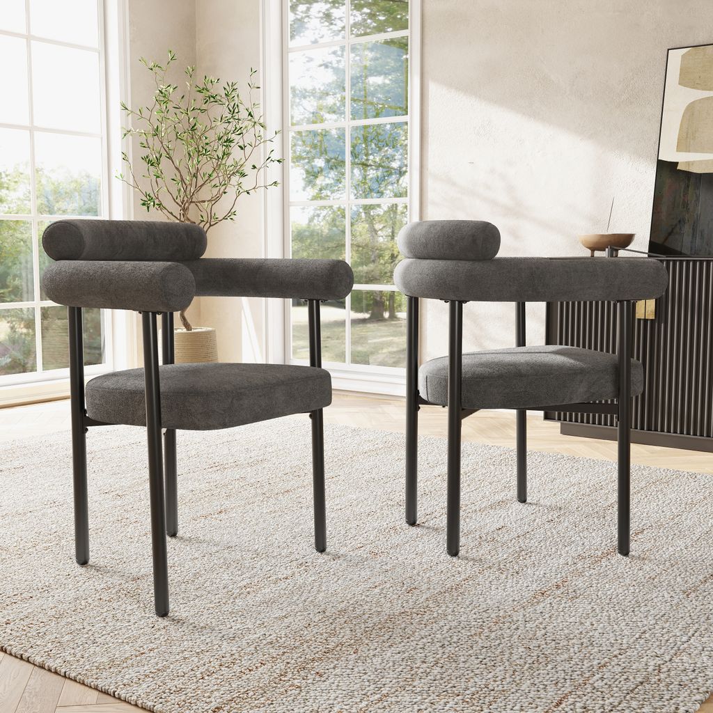 Two dark gray upholstered chairs with black metal legs are placed on a light-colored rug in a well-lit room with large windows.